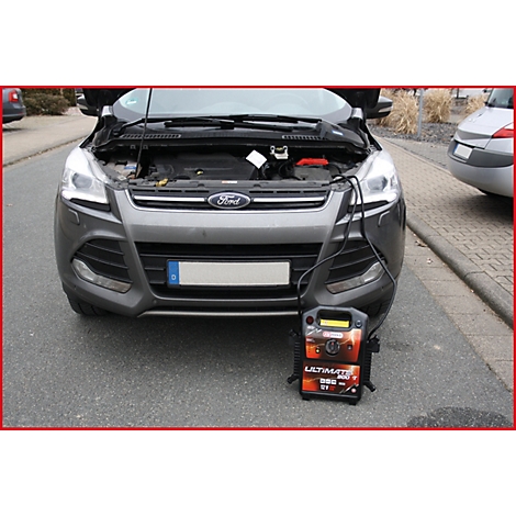 Ein grauer Ford Kuga mit geöffneter Motorhaube wird mit einem mobilen Starthilfe-Gerät aufgeladen. Schwarze Kabel verbinden beide Geräte.